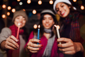 Three women hold candles. there are lights behind them.