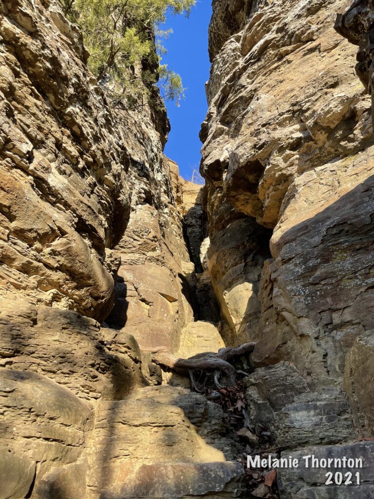 Looking upward toward a crevice in the side of the mountain with bright blue sky peaking through