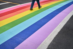 The legs of a person walking on a rainbow painted on a crosswalk