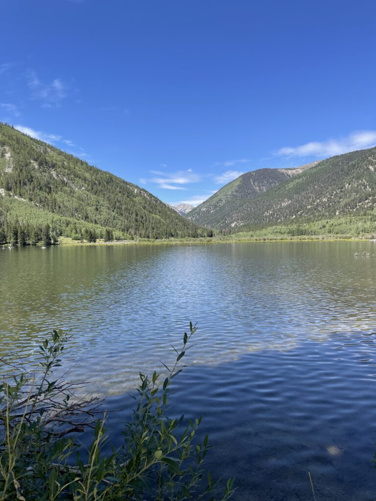 Ripples move across a large lake that is nestled between two mountain ridges. The bright blue sky above is reflected in the water below.